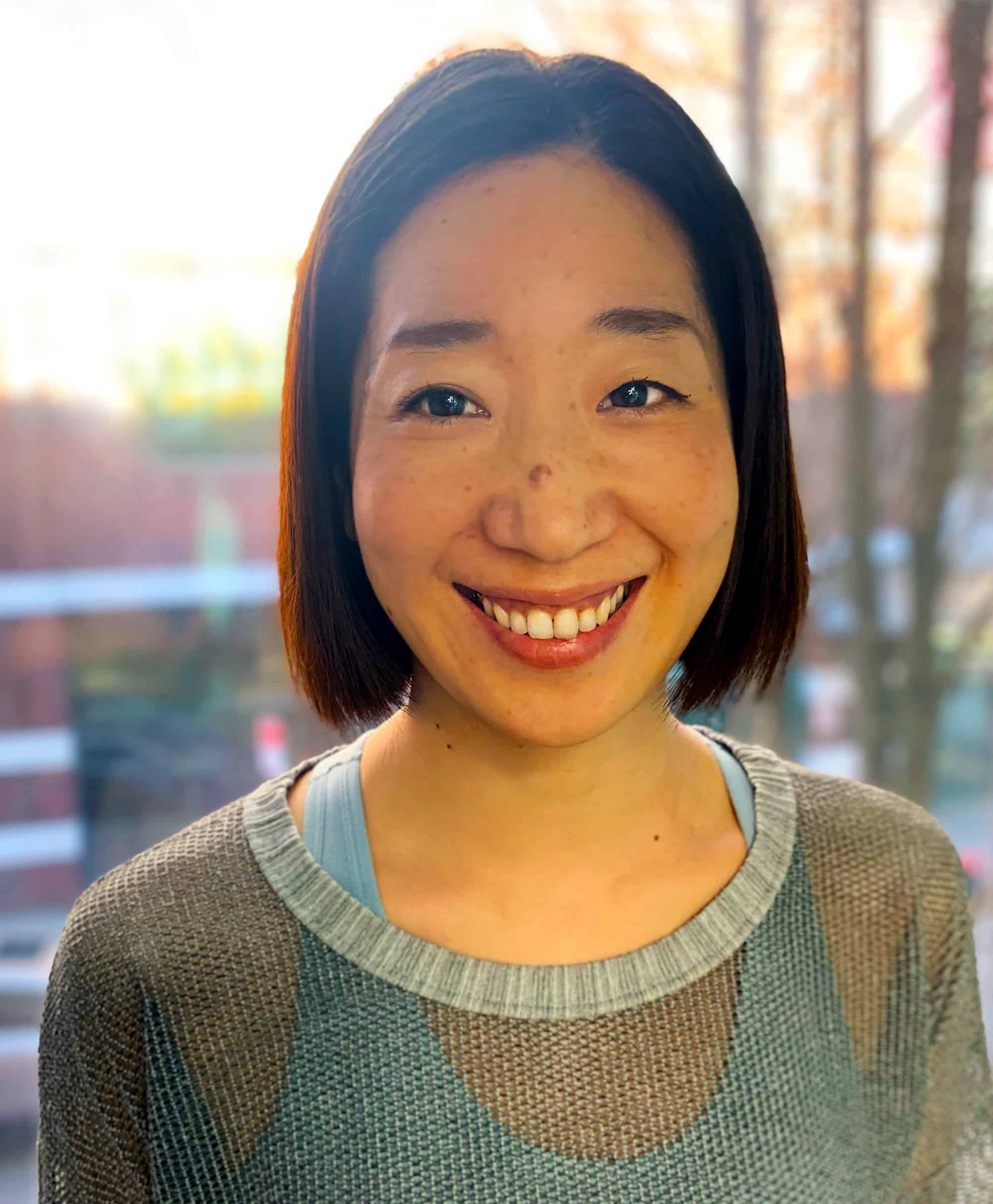 Portrait of Pilates Instructor Maho Ogawa with window and sunset behind her.